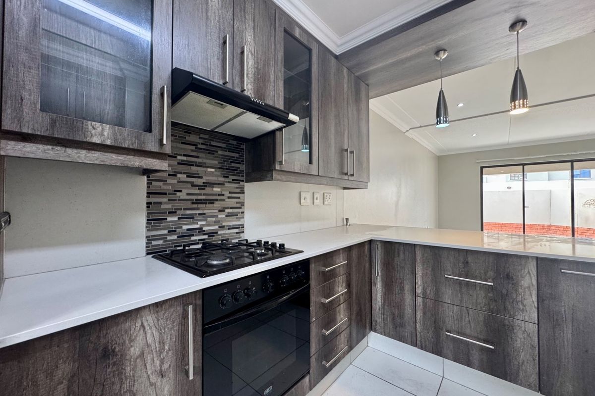 Modern kitchen featuring dark wood-grain cabinetry, stone countertops, a gas hob with extractor fan, and a stylish mosaic tile backsplash.