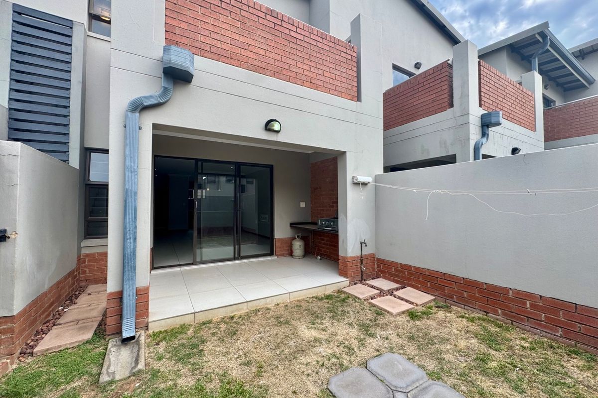 Rear view of the townhouse featuring a covered tiled patio with a built-in braai, sliding door access, and a small private garden area.