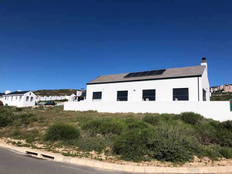 A modern residential property featuring a white facade, tiled roof with integrated solar panels, and a surrounding boundary wall in a coastal setting.