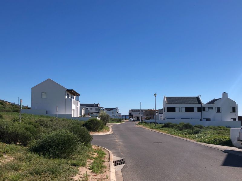 A clear street view of a residential neighborhood featuring paved roads, street lighting, and modern white homes with dark roofs.