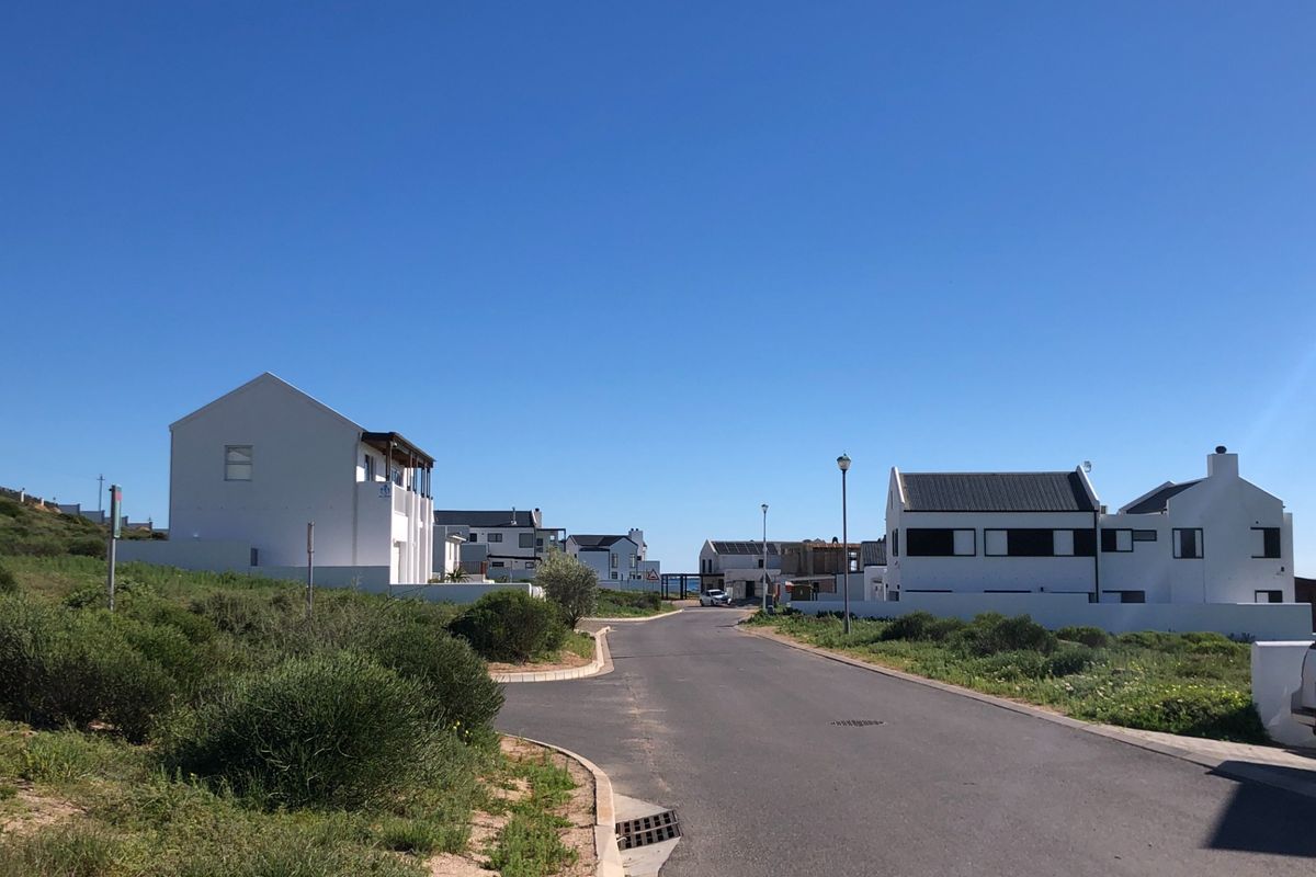 A clear street view of a residential neighborhood featuring paved roads, street lighting, and modern white homes with dark roofs.