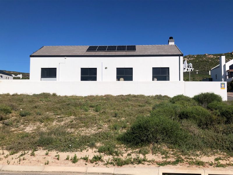 Rear view of a modern residential property featuring a white facade, tiled roof with solar panels, and a surrounding boundary wall.