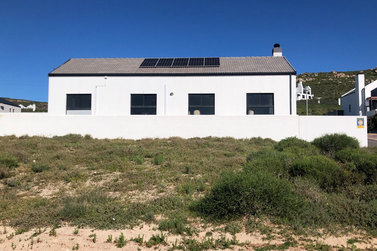 Rear view of a modern residential property featuring a white facade, tiled roof with solar panels, and a surrounding boundary wall.
