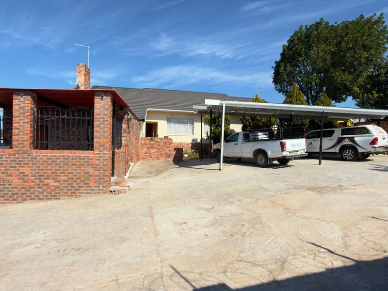 Front exterior view of the property featuring a concrete driveway, metal carport structure, and brick boundary walling.