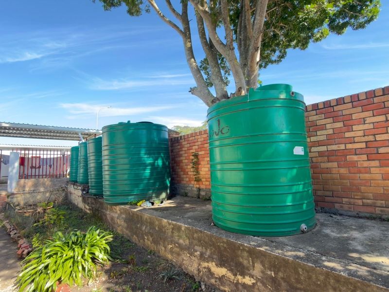 Rear exterior area featuring multiple green water storage tanks positioned on a concrete plinth against a brick boundary wall.