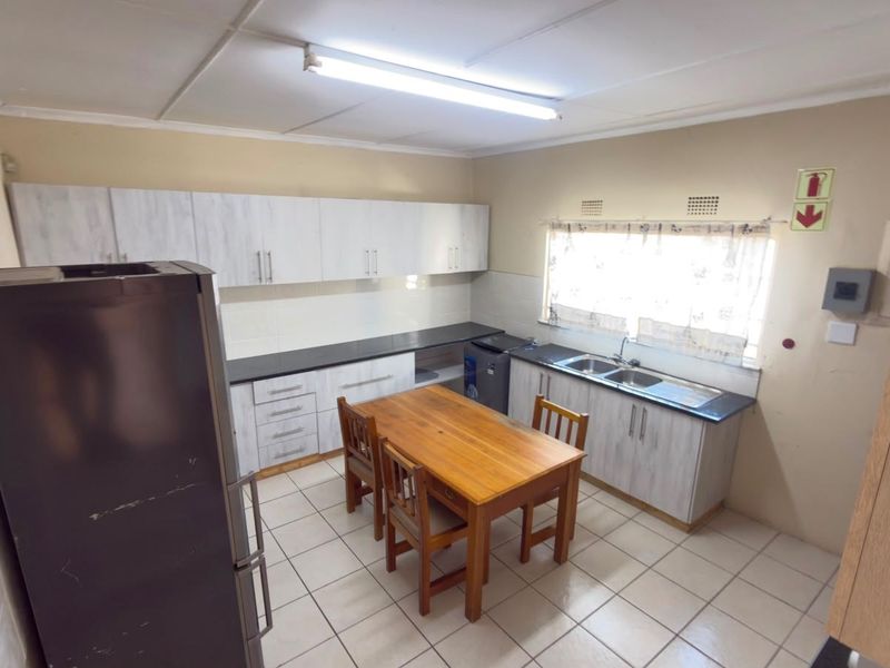 Functional kitchen featuring built-in cabinetry, double basin sink, tiled backsplash, and tiled flooring with ample space for a dining area.