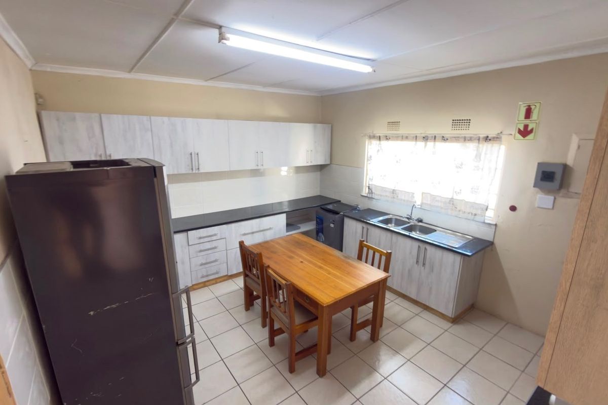 Functional kitchen featuring built-in cabinetry, double basin sink, tiled backsplash, and tiled flooring with ample space for a dining area.