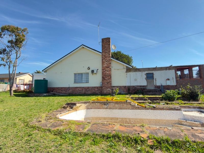 Rear view of the property featuring a swimming pool, brick chimney, and water tank, set within a large garden area requiring maintenance.