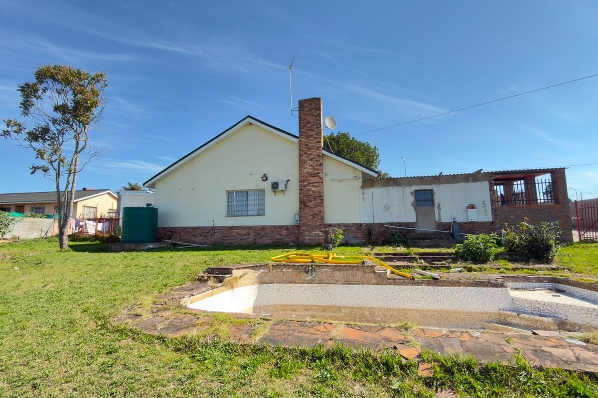 Rear view of the property featuring a swimming pool, brick chimney, and water tank, set within a large garden area requiring maintenance.