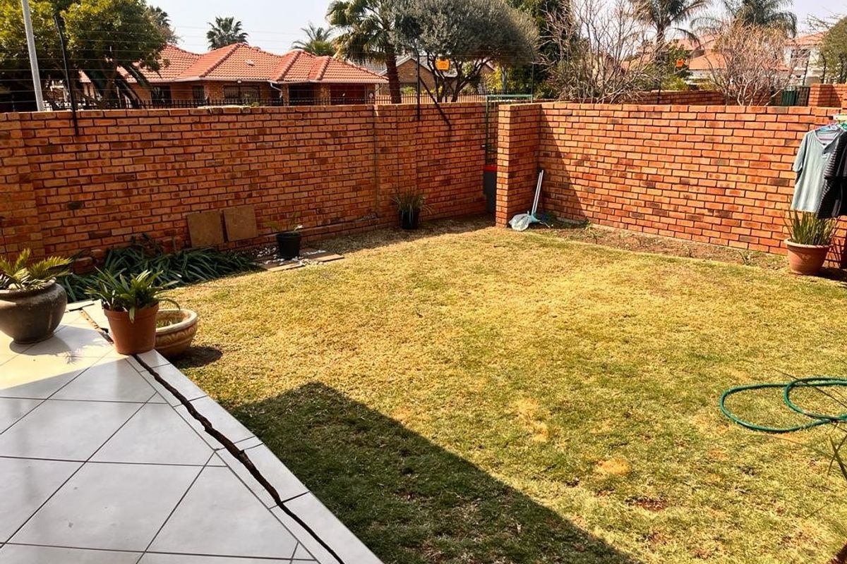A private rear garden featuring a tiled patio area, a lawn, and secure brick boundary walls with electric fencing.
