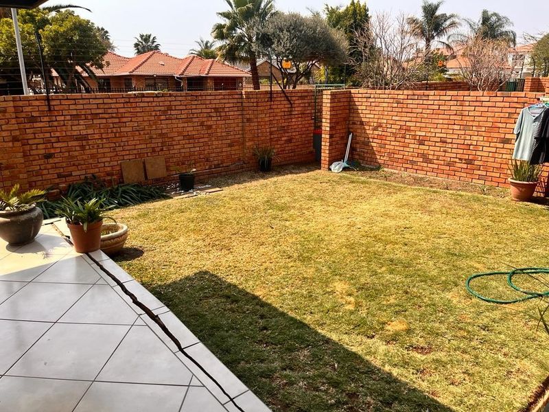 A private rear garden featuring a tiled patio area, a lawn, and secure brick boundary walls with electric fencing.