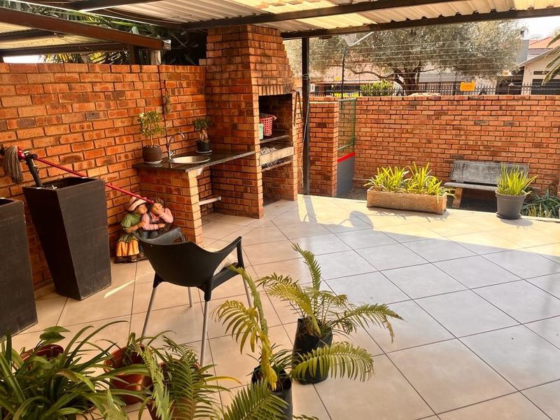 Covered outdoor patio featuring a built-in brick braai, granite prep area with sink, and tiled flooring, ideal for entertaining.
