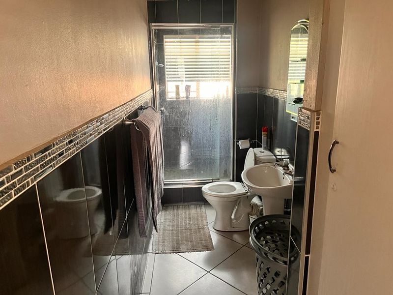 A functional bathroom featuring a pedestal basin, toilet, and a glass-enclosed shower with dark tiled walls and flooring.