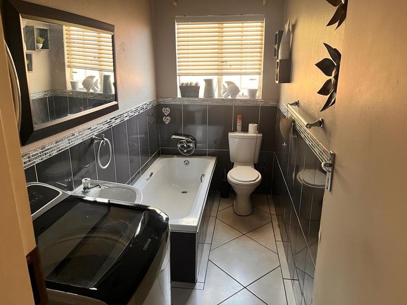 A functional bathroom featuring a bathtub, toilet, and washbasin with dark tiled walls and tiled flooring.
