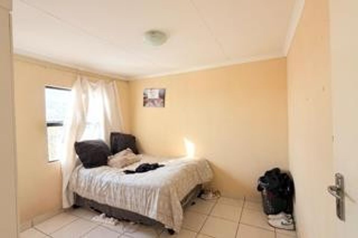 A simple bedroom featuring tiled flooring and a standard window, offering a functional space that would benefit from cosmetic updates and fresh paint.