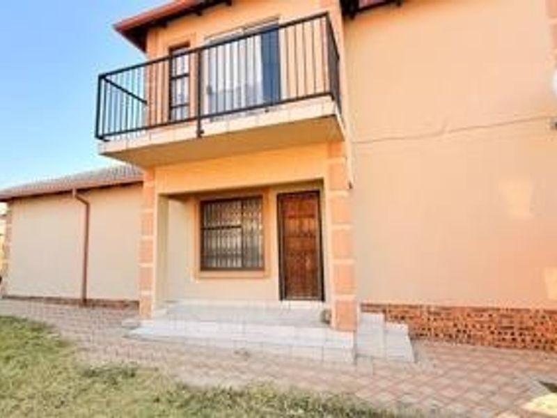 Rear view of the house featuring a paved patio area, a first-floor balcony with metal railings, and security features on windows and doors.