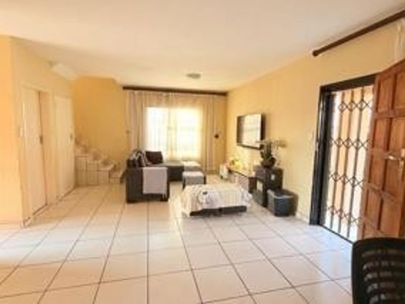 Spacious living area featuring tiled flooring, a staircase, and direct access to the exterior through a secure timber door.