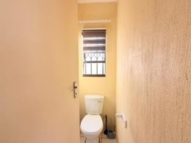 A compact guest bathroom featuring a standard toilet, a window with security bars, and a roller blind.