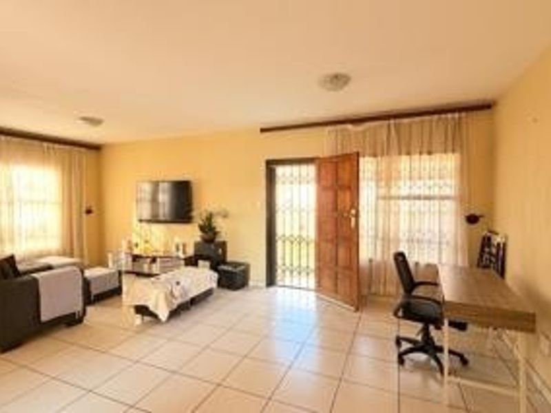 Spacious living area featuring neutral tiled flooring, large windows with curtain rails, and direct access to the exterior via a secure wooden door.