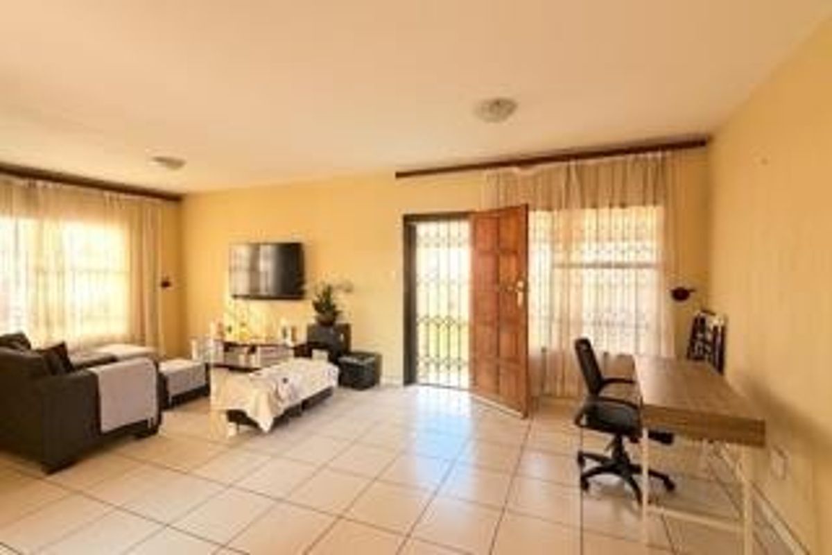 Spacious living area featuring neutral tiled flooring, large windows with curtain rails, and direct access to the exterior via a secure wooden door.