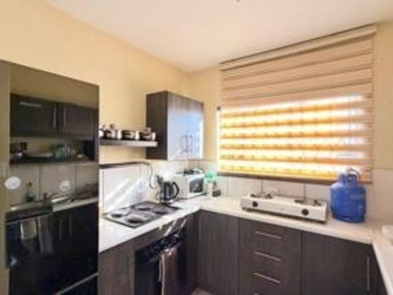 A functional kitchen featuring dark wood cabinetry, a built-in oven and hob, and a double sink with natural light provided by a window.