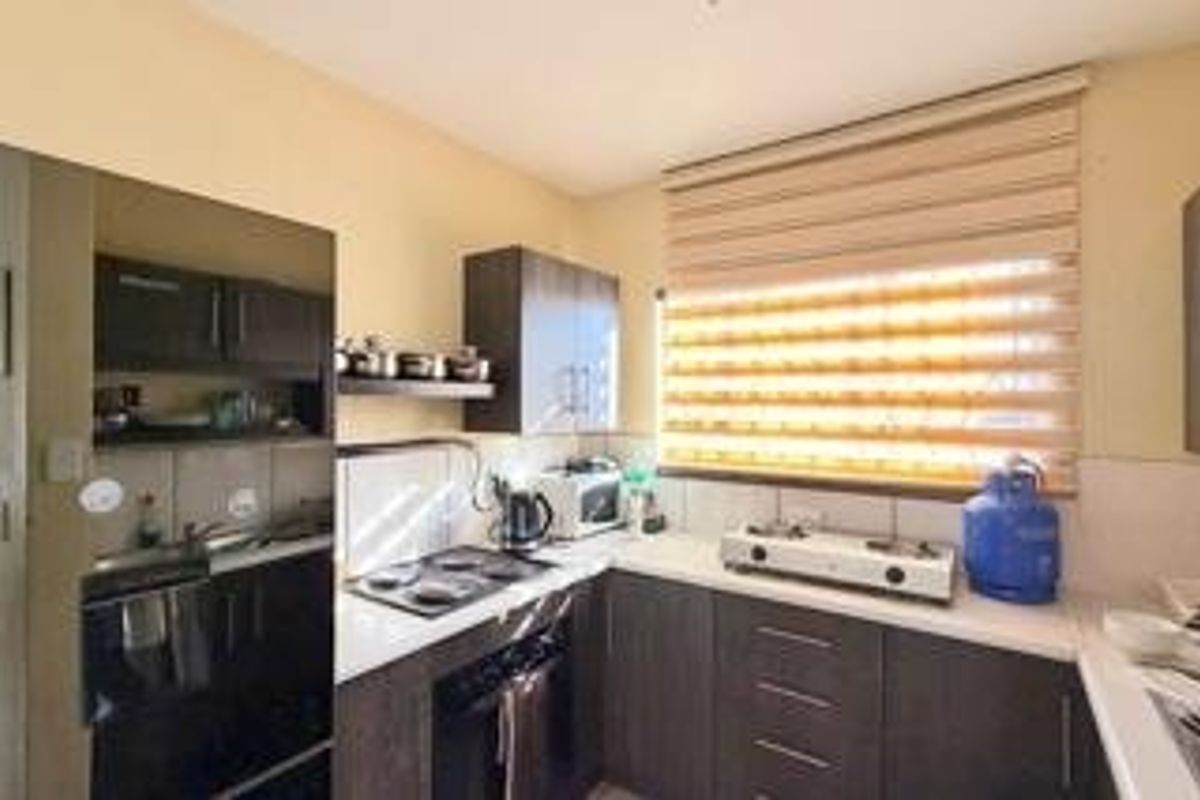 A functional kitchen featuring dark wood cabinetry, a built-in oven and hob, and a double sink with natural light provided by a window.