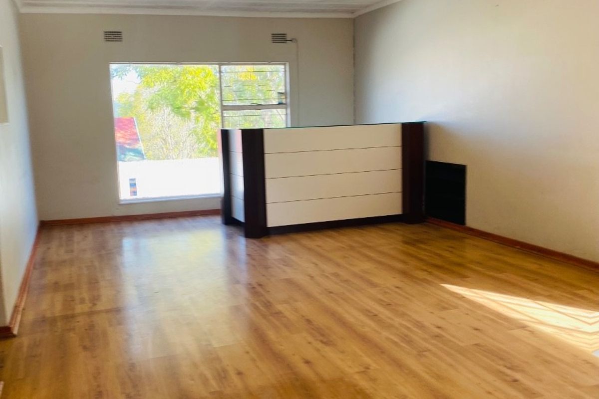 A spacious, empty living area featuring warm-toned laminate flooring, neutral walls, and a large window providing natural light.