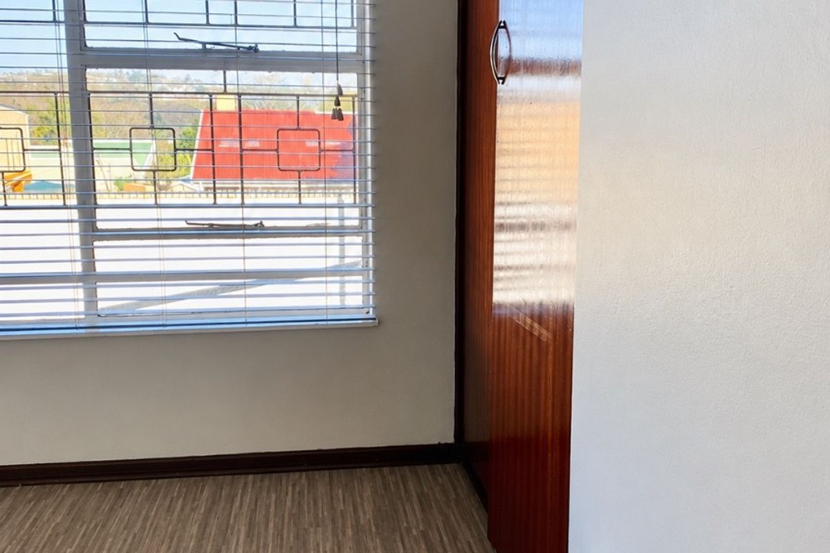 A bright, empty bedroom featuring laminate flooring, a built-in wooden wardrobe, and a window fitted with security bars.