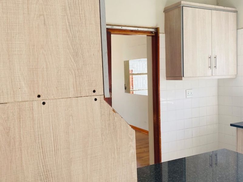 A kitchen area featuring light wood-look cabinetry, dark granite countertops, and white tiled backsplash, showing signs of wear and unfinished cabinet installation.