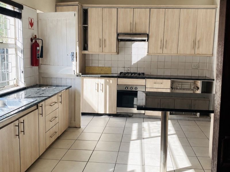 A functional kitchen featuring light wood cabinetry, granite countertops, a gas hob, and tiled flooring, offering a clean space ready for modern updates.