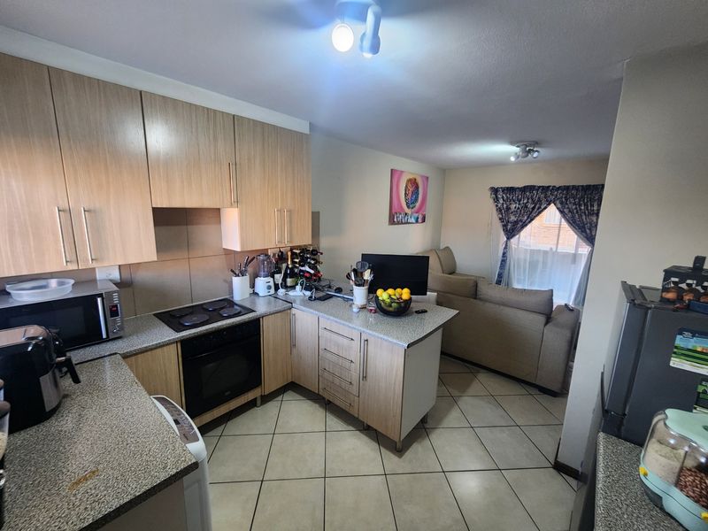 Open plan kitchen and living area featuring light wood cabinetry, granite countertops, built-in oven, electric hob, and tiled flooring throughout.