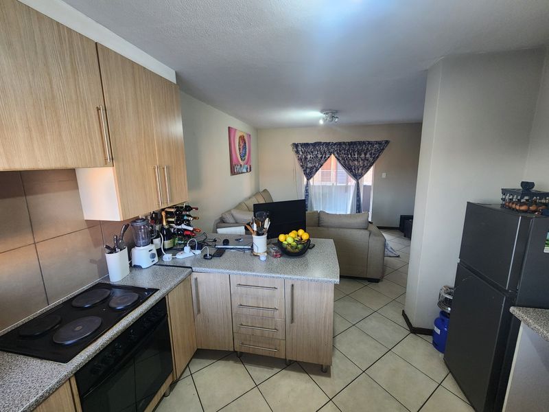 Open-plan kitchen and living area featuring wood-look cabinetry, laminate countertops, electric hob, and tiled flooring leading to a balcony.