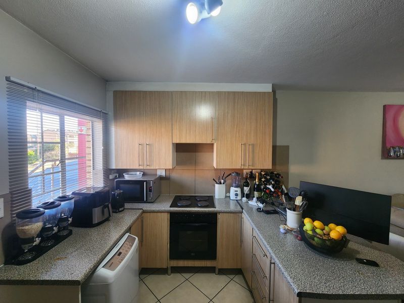 Compact kitchen featuring light wood-finish cabinetry, granite countertops, built-in oven, electric hob, and tiled flooring, offering a functional layout for daily meal preparation.