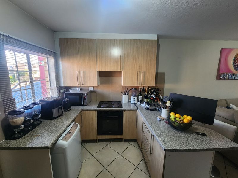 A functional U-shaped kitchen featuring light wood-finish cabinetry, granite countertops, built-in electric oven and hob, and tiled flooring.