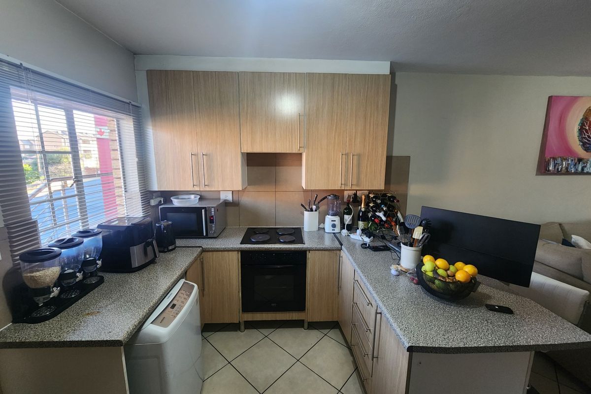 A functional U-shaped kitchen featuring light wood-finish cabinetry, granite countertops, built-in electric oven and hob, and tiled flooring.