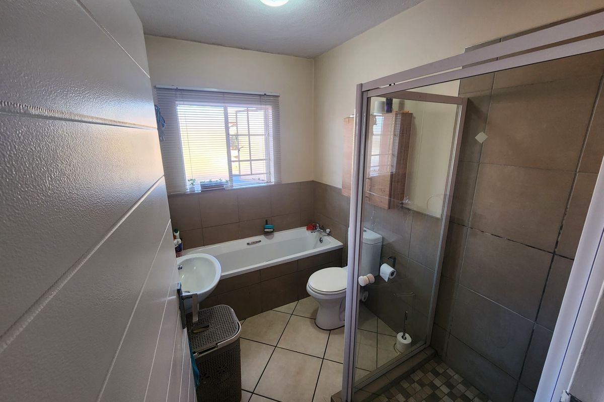A functional bathroom featuring a bathtub, separate shower enclosure, pedestal basin, and toilet with neutral wall and floor tiling.