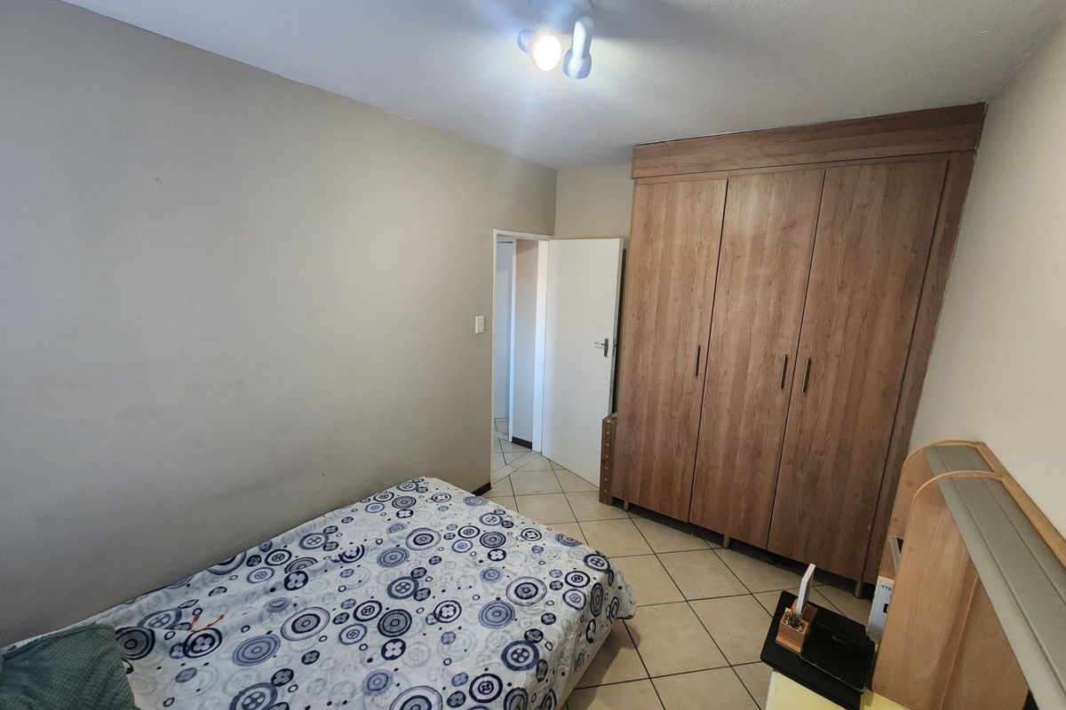 A functional bedroom featuring tiled flooring and a large built-in wooden wardrobe, providing ample storage space.
