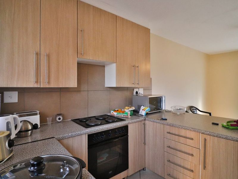 Functional kitchen featuring light wood-finish cabinetry, stone-look laminate countertops, a built-in oven, and an electric hob with a tiled backsplash.