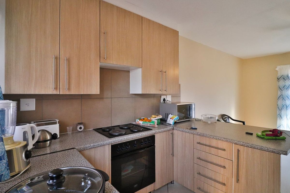Functional kitchen featuring light wood-finish cabinetry, stone-look laminate countertops, a built-in oven, and an electric hob with a tiled backsplash.
