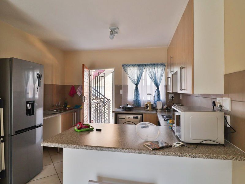 A functional kitchen featuring laminate cabinetry, stone-look countertops, tiled backsplash, and direct access to an exterior security gate.