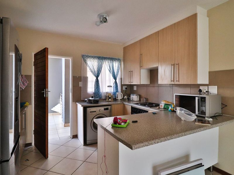 A functional kitchen featuring light wood-finish cabinetry, stone-look countertops, a built-in hob and oven, and integrated laundry space with tiled flooring.