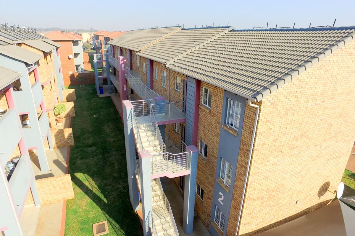 Aerial view of a multi-story apartment complex featuring brick facades, tiled roofs, external staircases, and communal landscaped garden areas.