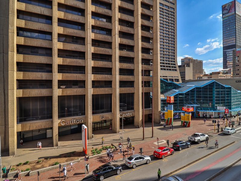 Elevated street-level view of the Carlton Centre commercial building facade, featuring concrete architecture and integrated retail entrance areas.