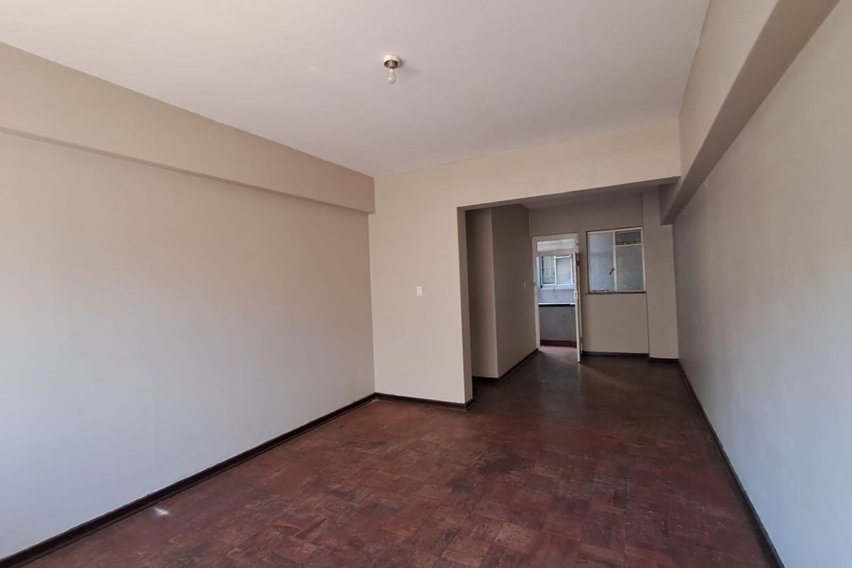 An empty living room featuring original parquet flooring and neutral wall finishes, offering a blank canvas for renovation and interior design.