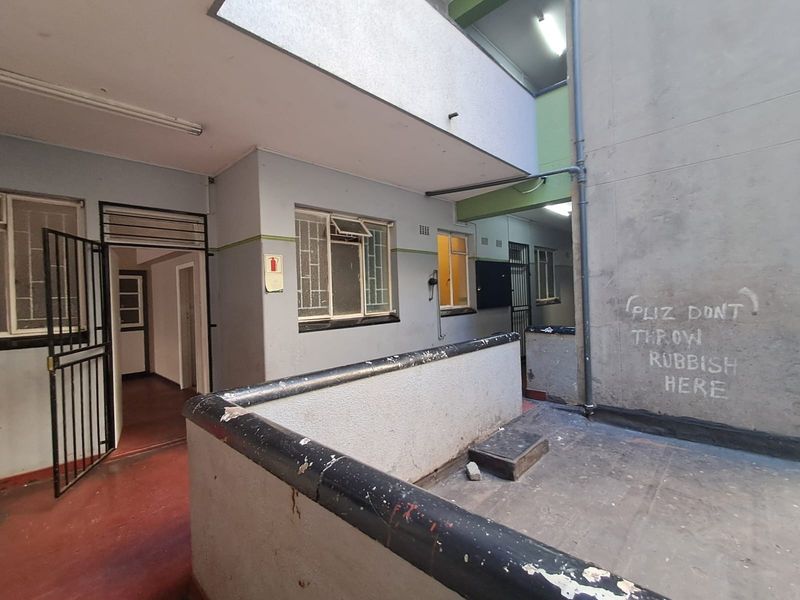 An exterior common area or walkway of an apartment building featuring concrete balustrades, security gates, and visible wear on the building facade.