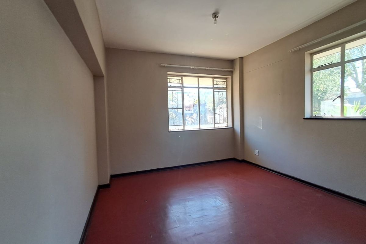 An empty bedroom featuring painted concrete floors, neutral walls, and windows fitted with metal security bars.