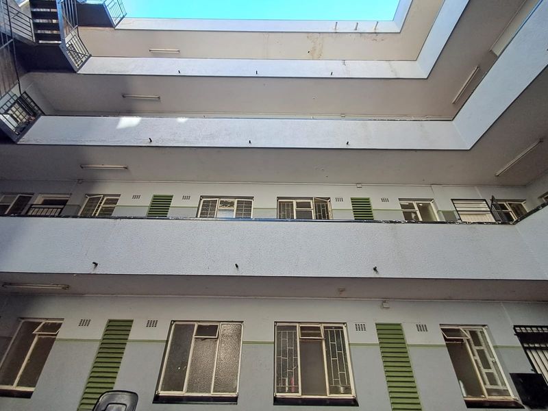 Upward view of an apartment building courtyard featuring multi-level balcony walkways, metal window frames with security bars, and visible exterior wall wear.