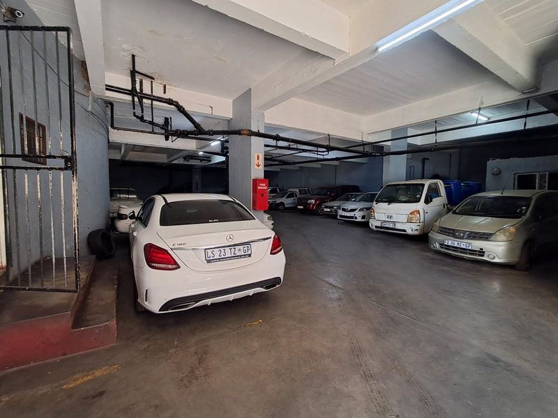 A functional underground parking garage featuring concrete flooring, exposed overhead utility pipes, and structural support columns.