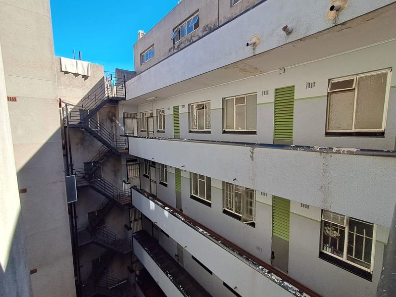 Exterior view of an apartment building showing multi-level walkways, metal fire escape stairs, and standard window configurations with security bars.