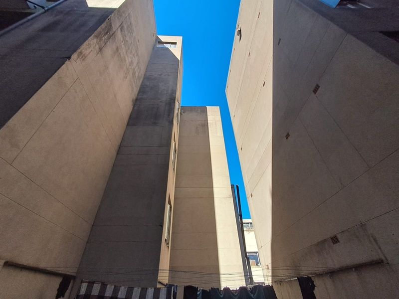 View looking up between apartment building blocks showing concrete exterior facades with visible weathering and staining.